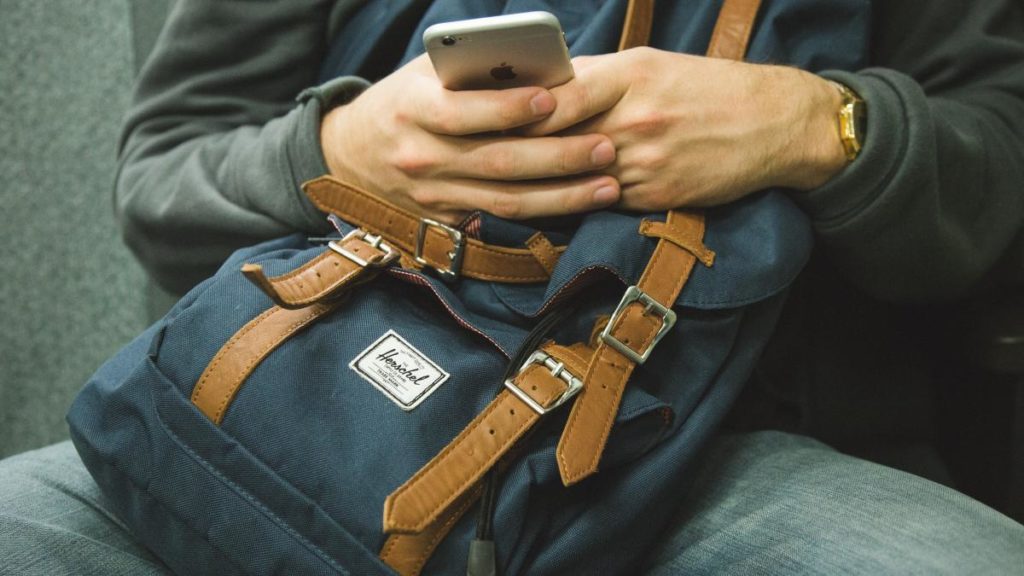 Man holding iPhone and Herschel Backpack | Free Airport WiFi Passwords