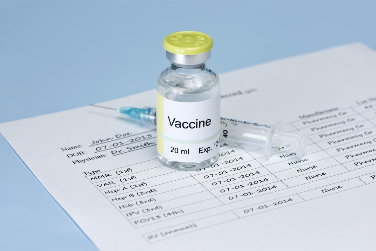  A vaccination record form with a syringe and vial of vaccine, illustrating the need for travel vaccinations to stay safe and healthy while traveling.